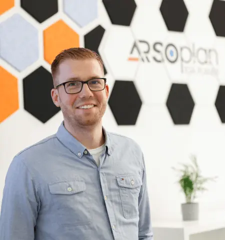 Marvin Adrian im ARSOplan-Büro vor dem Firmenlogo